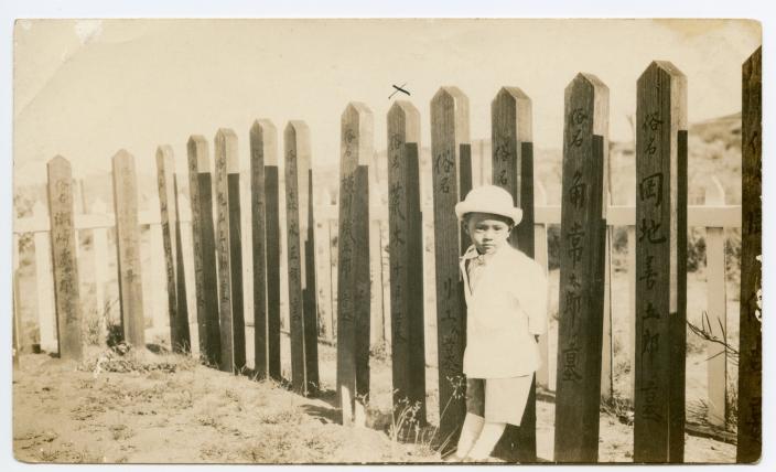 A small boy leaning against  a fence. 